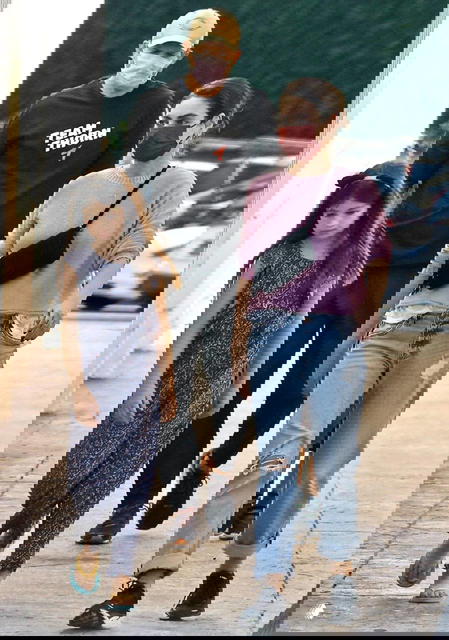 Мила Кунис, Эштон Кутчер и дочь идут по тротуару; снимок показывает прогулку семьи в масках и повседневной одежде.