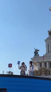 Две ведущие на синей дорожке у исторического здания на фоне ясного неба; у обеих заметны элементы зебрового принта в образах.