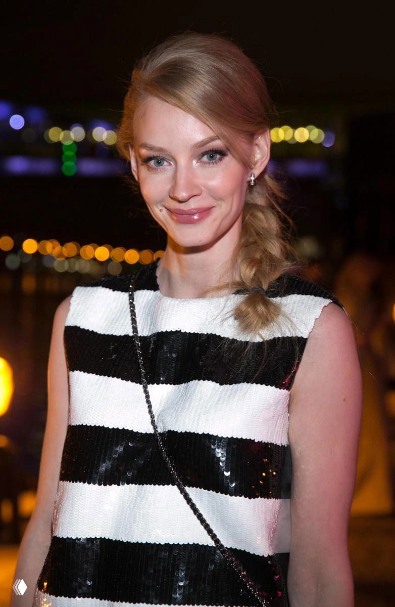 Крупный план улыбки женщины в чёрно‑белой полосатой одежде на вечернем приёме, боке огней и мягкое освещение создают тёплую атмосферу.