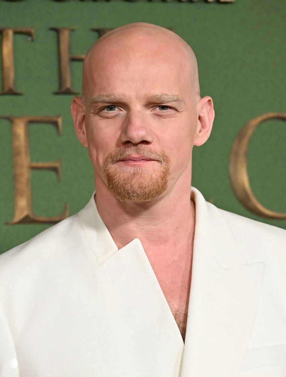 Крупный план лица мужчины с короткой бородой на фоне зелёного пресс-волла — профессиональный портрет с премьеры или фотоколла.