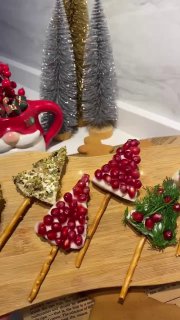 Готовые закуски в виде новогодних елочек: крендельные палочки, крем, зелёная глазурь и зерна граната на сервировочной доске.