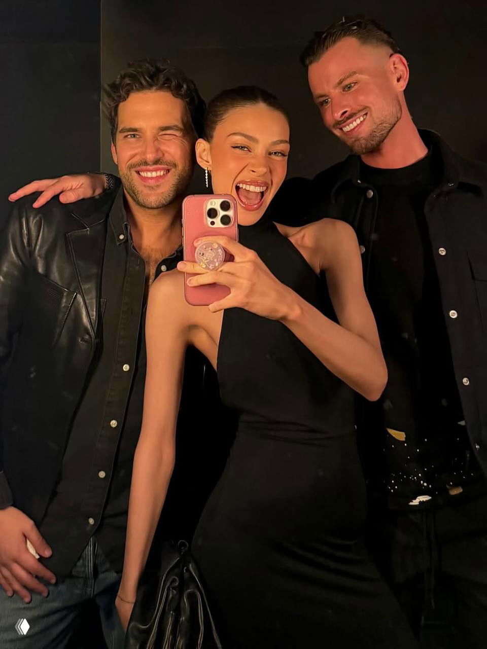Никола Пельтц смеётся в селфи с двумя мужчинами на вечеринке; все в тёмной одежде, праздничное настроение и близкий план