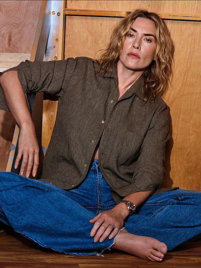 Женщина в рубашке и джинсах, расслабленная поза на полу студии, естественные выражения и тёплая цветовая палитра съёмки.