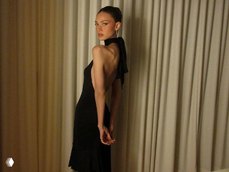 Никола Пельтц в чёрном облегающем платье в полный рост; позирует для фото на вечеринке, акцент на образе и худобе