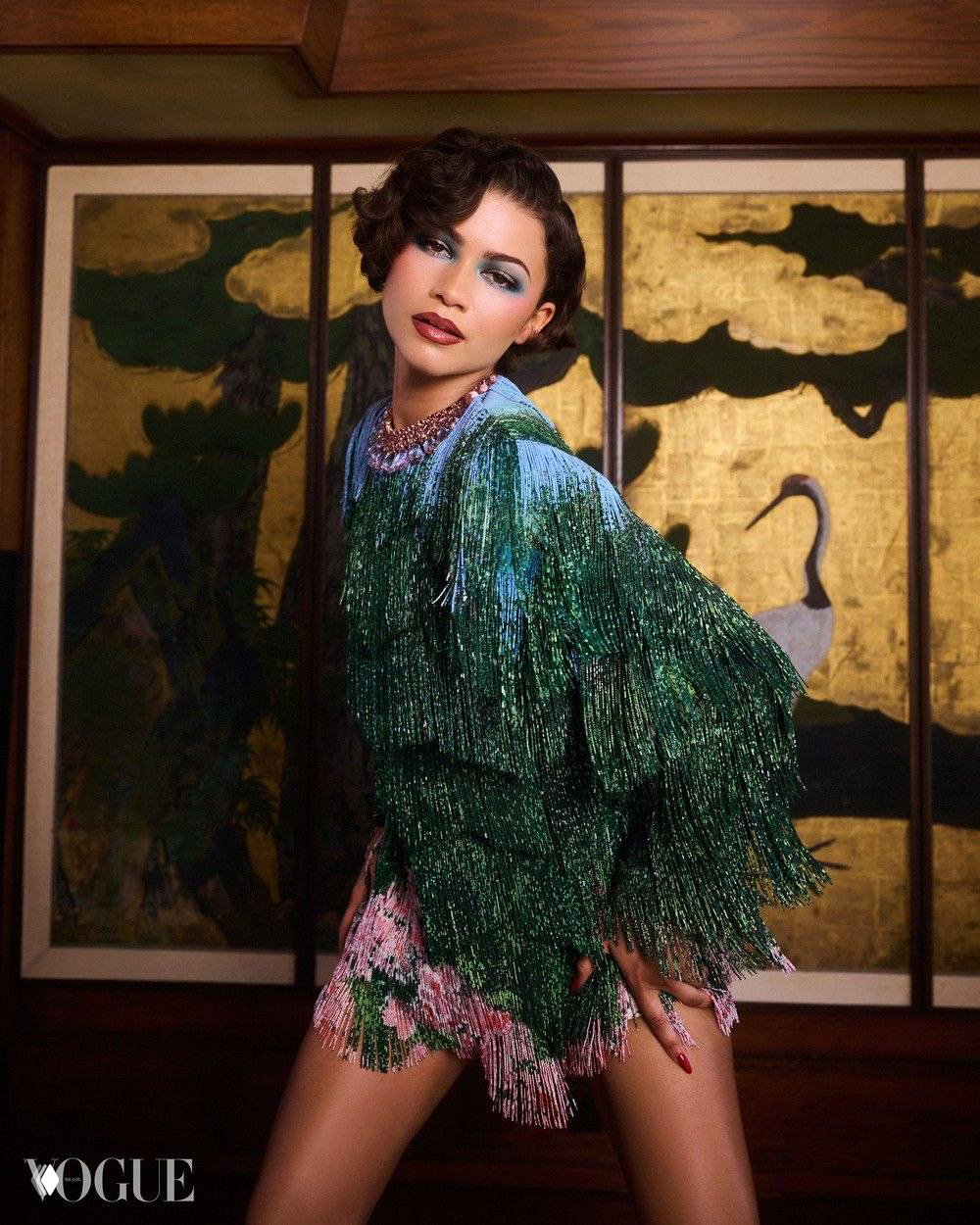 Фотосессия Зендеи в студии для Vogue Brasil: зелёное блестящее платье с бахромой на фоне декоративной ширмы с журавлями, гламурный кадр.