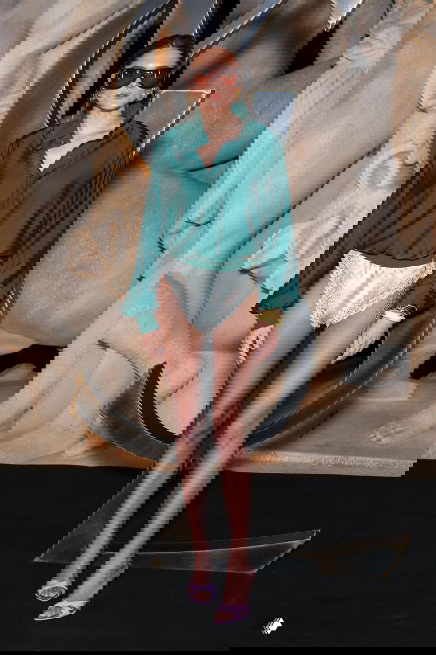 Модель в зелёной атласной рубашке, светлых шёлковых трусиках-комбинации и тонких босоножках позирует у арт-инсталляции Saint Laurent в Париже.