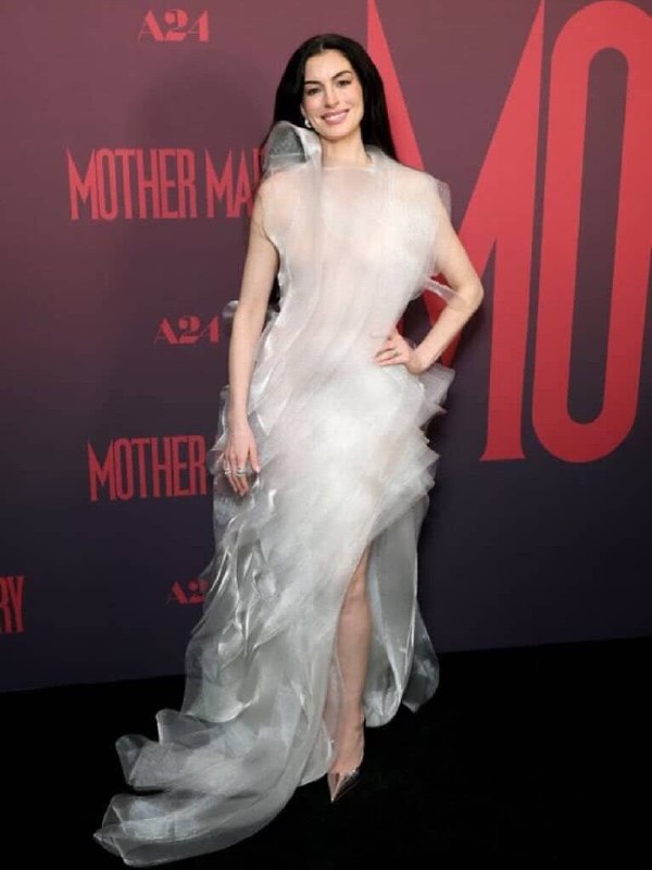 Кадр в полный рост: длинное слоистое белое платье с шлейфом на премьере, видно прозрачную фактуру ткани и острые туфли.