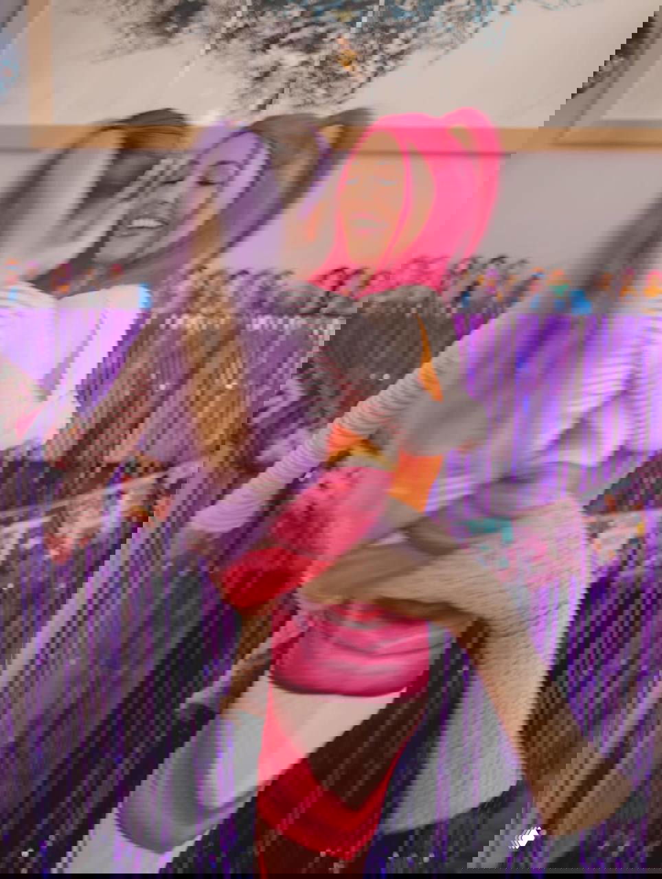 Женщина с ярко-розовыми прядями весело обнимает ребёнка в фиолетовой праздничной декорации, кадр в движении на дне рождения.