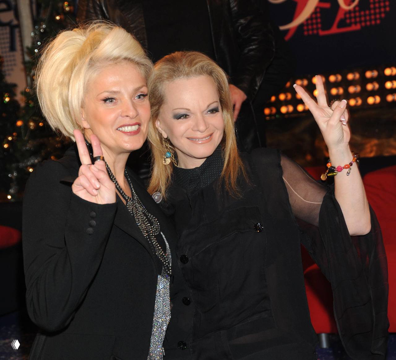 Лайма Вайкуле и подруга улыбаются и показывают знак V: тёплое фото в студийной или вечерней обстановке, дружеская поза и наряды.