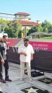 Турецкий певец Edis в белой рубашке и светлых брюках стоит у плитки Sea Breeze Walk of Fame на открытии звезды в Баку, рядом охрана и красная дорожка.