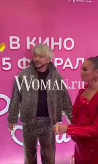 Филипп Киркоров и Ольга Бузова на розовой фотозоне премьеры «Равиоли Оли», Киркоров в светлом костюме, на фоне виден логотип Woman.ru