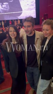 Группа гостей в кинозале на премьерном показе: мужчина в центре и женщины по бокам, улыбки и вечерняя одежда на фоне сцены