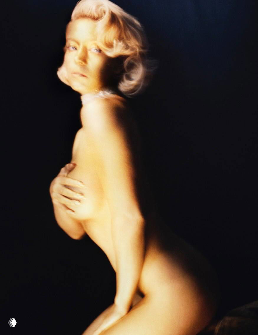 Портрет Сидни Суини в ретро‑образе: актриса в профиль прикрывает грудь рукой, мягкое размытие и свет на тёмном фоне.