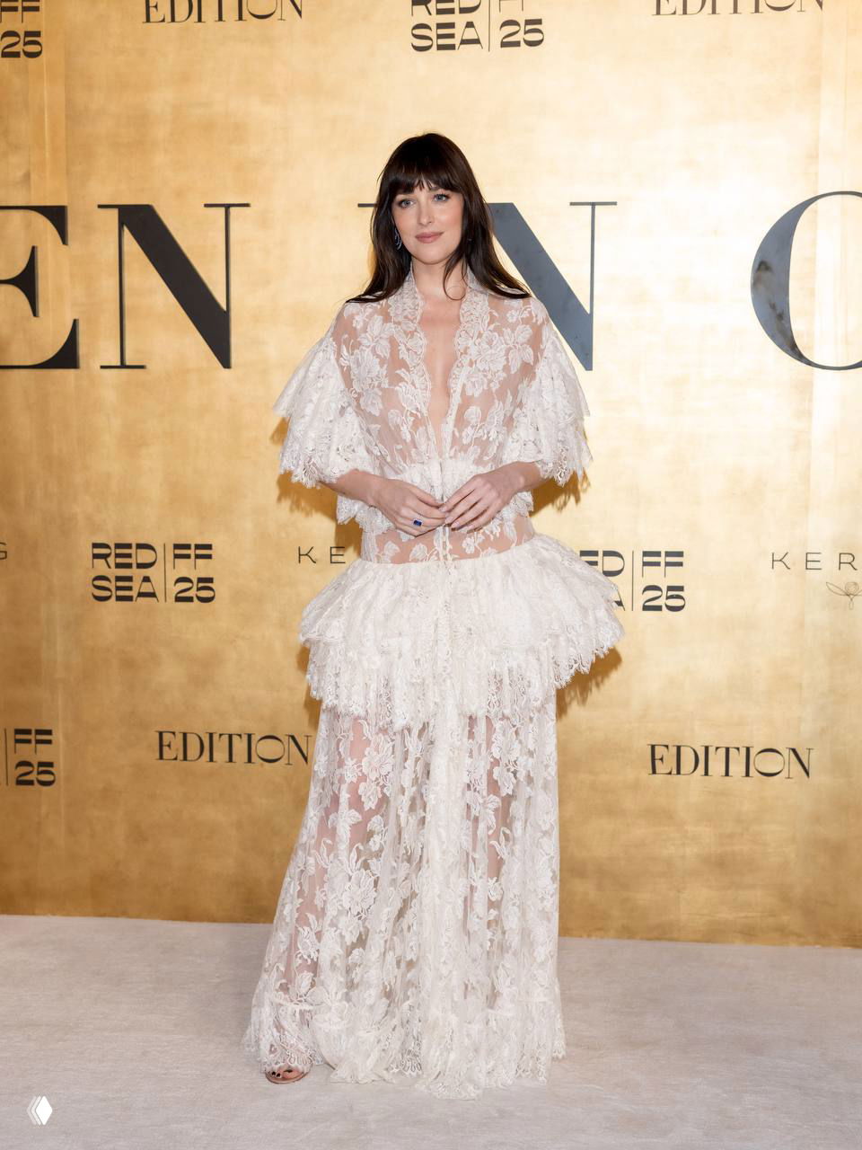 Женщина в многослойном белом кружевном платье с прозрачными элементами и короткой рюшей на талии; стильный и романтичный образ на светлом фоне.