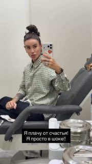 Айза делает фото в зеркале в кабинете клиники: полный рост в casual‑образе, видна обстановка клиники и результат после процедуры на лице.