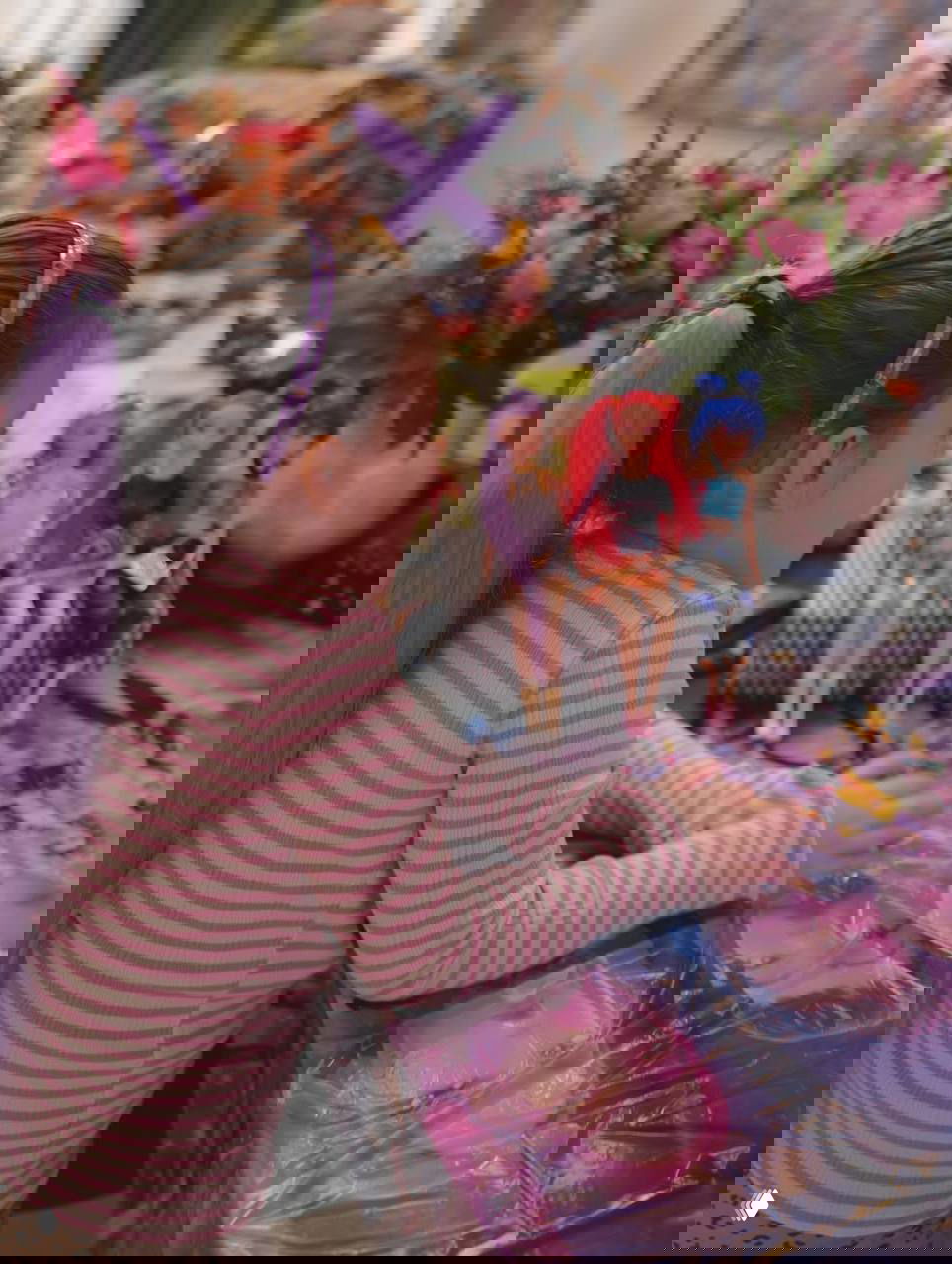 Ребёнок с фиолетовым хвостиком сидит за столом, перед ним куклы и подарки, видна праздничная сервировка и игрушки.