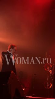 Музыкальный номер на сцене в красном освещении: исполнитель поёт в микрофон, видны световые эффекты и часть бэк‑составa