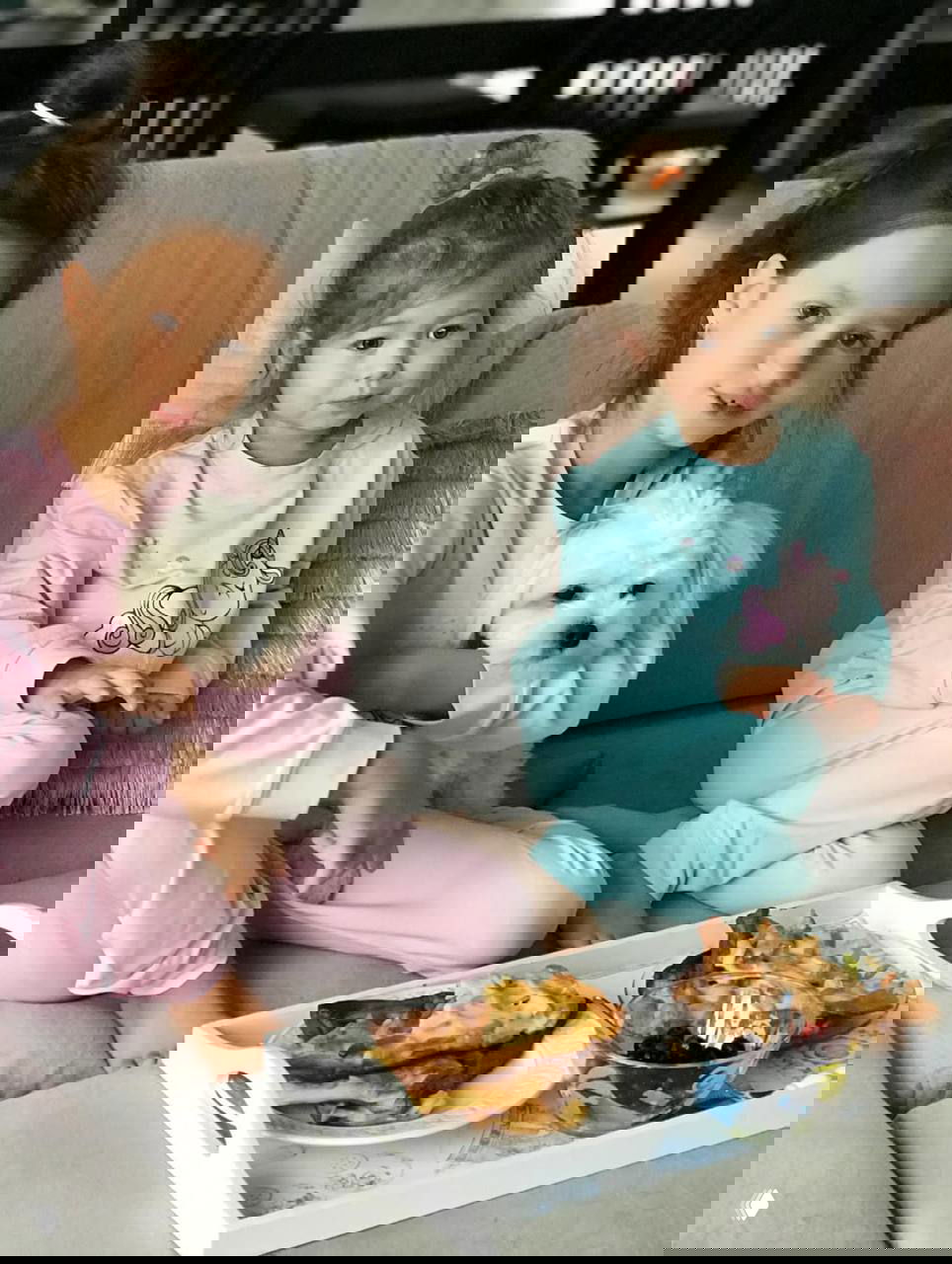 Две девочки в пижамах на диване с маленькой белой собакой и подносом с блинами — утренний семейный завтрак на дому.