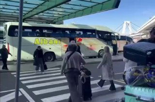 Пассажиры с чемоданами и дорожным багажом у рейсового автобуса на подходе к терминалу: люди с сумками и загруженная платформа.