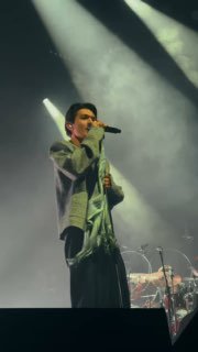 Исполнение песни с интенсивным прожекторным светом: певец держит микрофон, вокруг видны дым и элементы музыкальной сцены