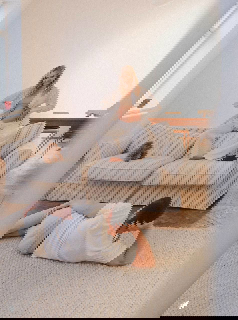 Ещё один общий план той же фотосессии: Даша на диване демонстрирует беременный живот, Никита рядом на полу, мягкое дневное освещение.