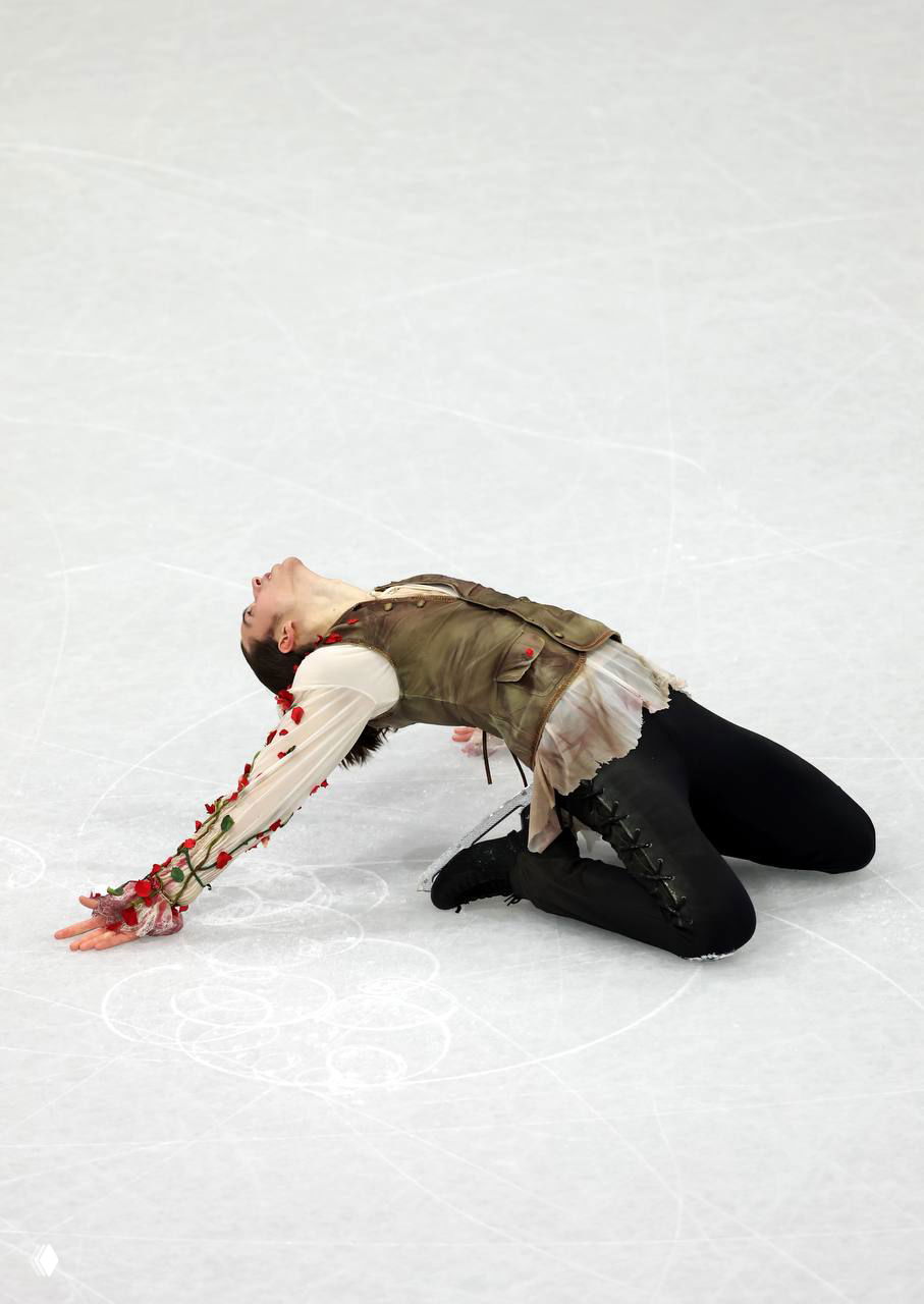 Пётр Гуменник в позе на коленях на льду, видно жилет и блузу с цветочной аппликацией — кадр из короткой программы.