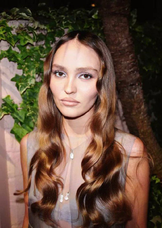 Крупный план лица Лили-Роуз Депп на вечеринке Chanel: выразительная мимика, длинные волнистые волосы и натуральный макияж.