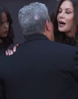 Кадр со съёмок события: Кэтрин Зета‑Джонс здоровается с Луисом Гусманом на красной дорожке, у обоих дружелюбные жесты и фон с тематикой шоу.