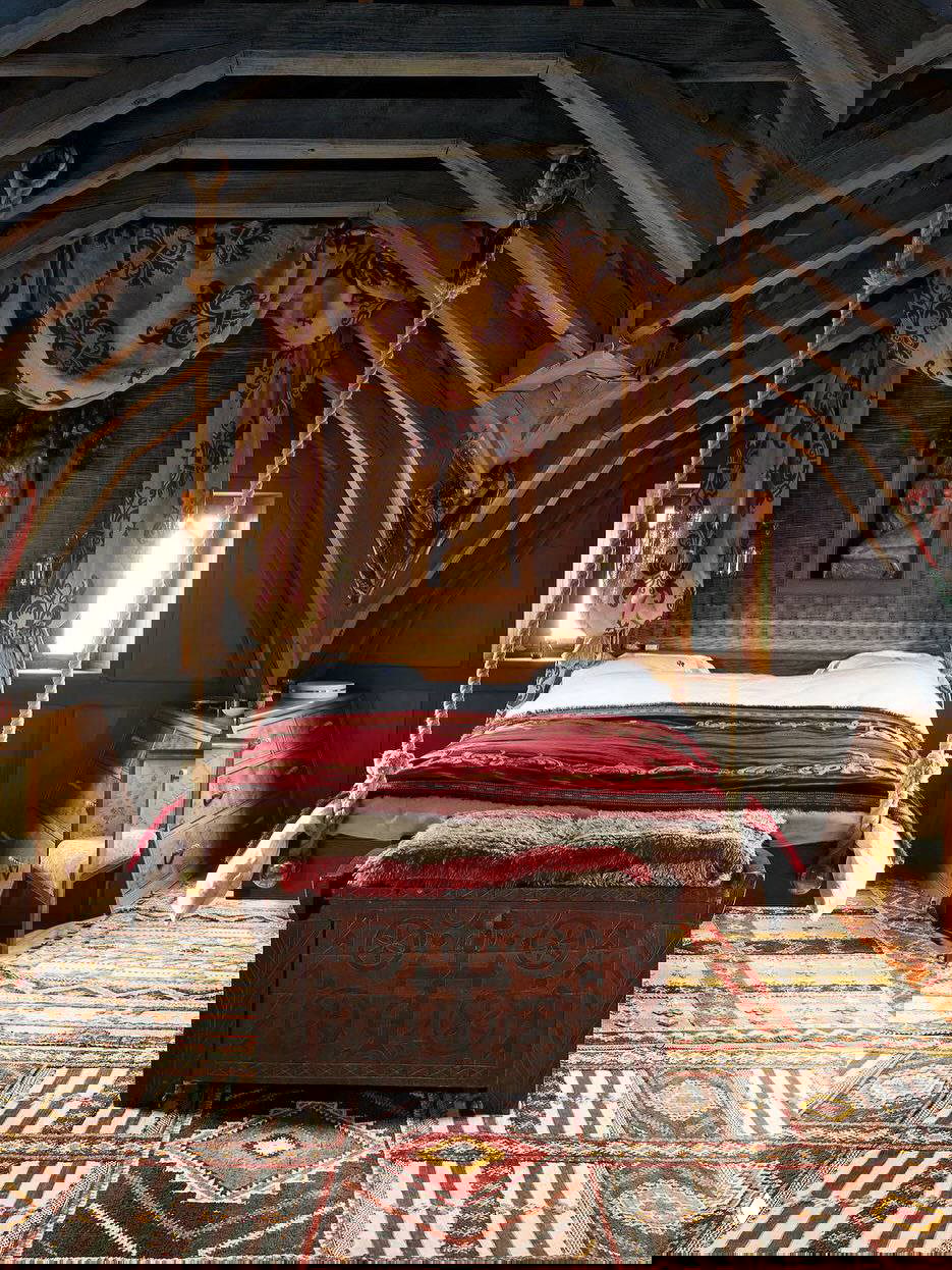 Спальня на мансарде замка с подвесной балдахинной кроватью, богато украшенным текстилем и старинным сундуком у ног кровати, атмосфера средневековой роскоши.