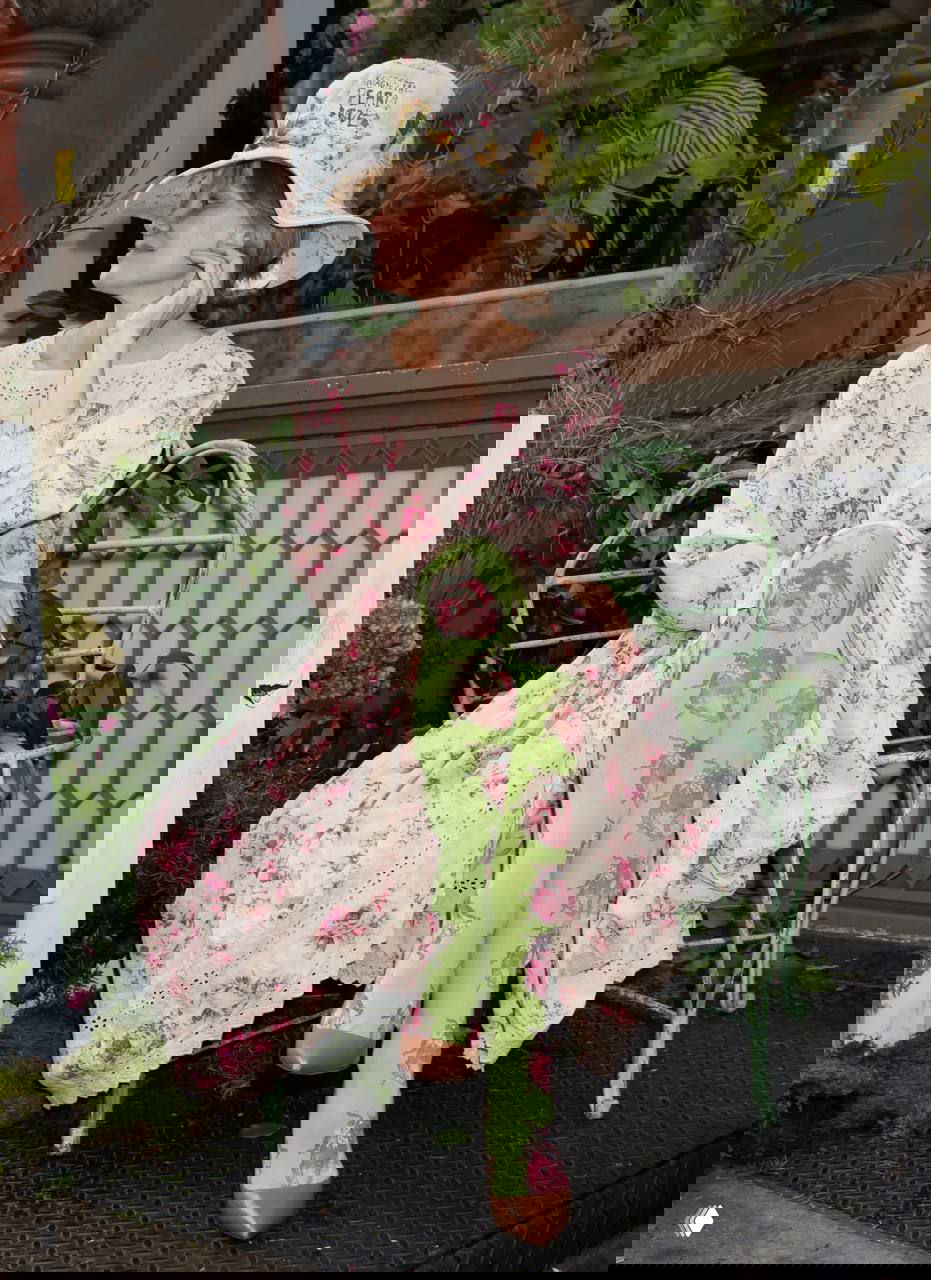 Памела в платье с розовым принтом сидит на декоративной скамье среди зелёных растений и цветочного декора pop-up магазина Sonsie.