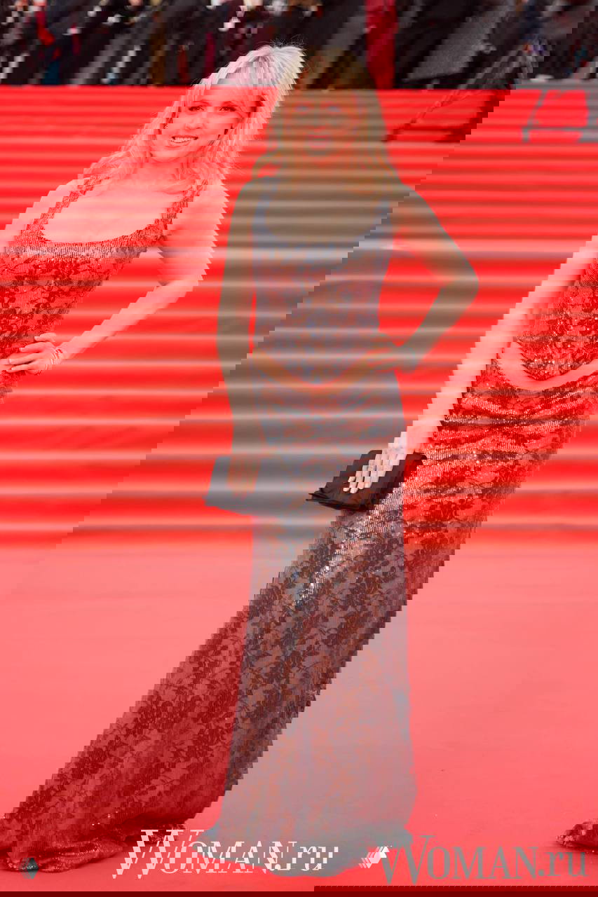 Женщина в блестящем платье с кружевным узором позирует на красной дорожке 48-го ММКФ, слышны щёлканья камер и суета прессы на заднем плане.