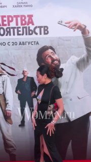 Женщина в чёрном платье идёт мимо большого постера фильма «Жертва обстоятельств» в коридоре кинотеатра во время показа и фотосессии.