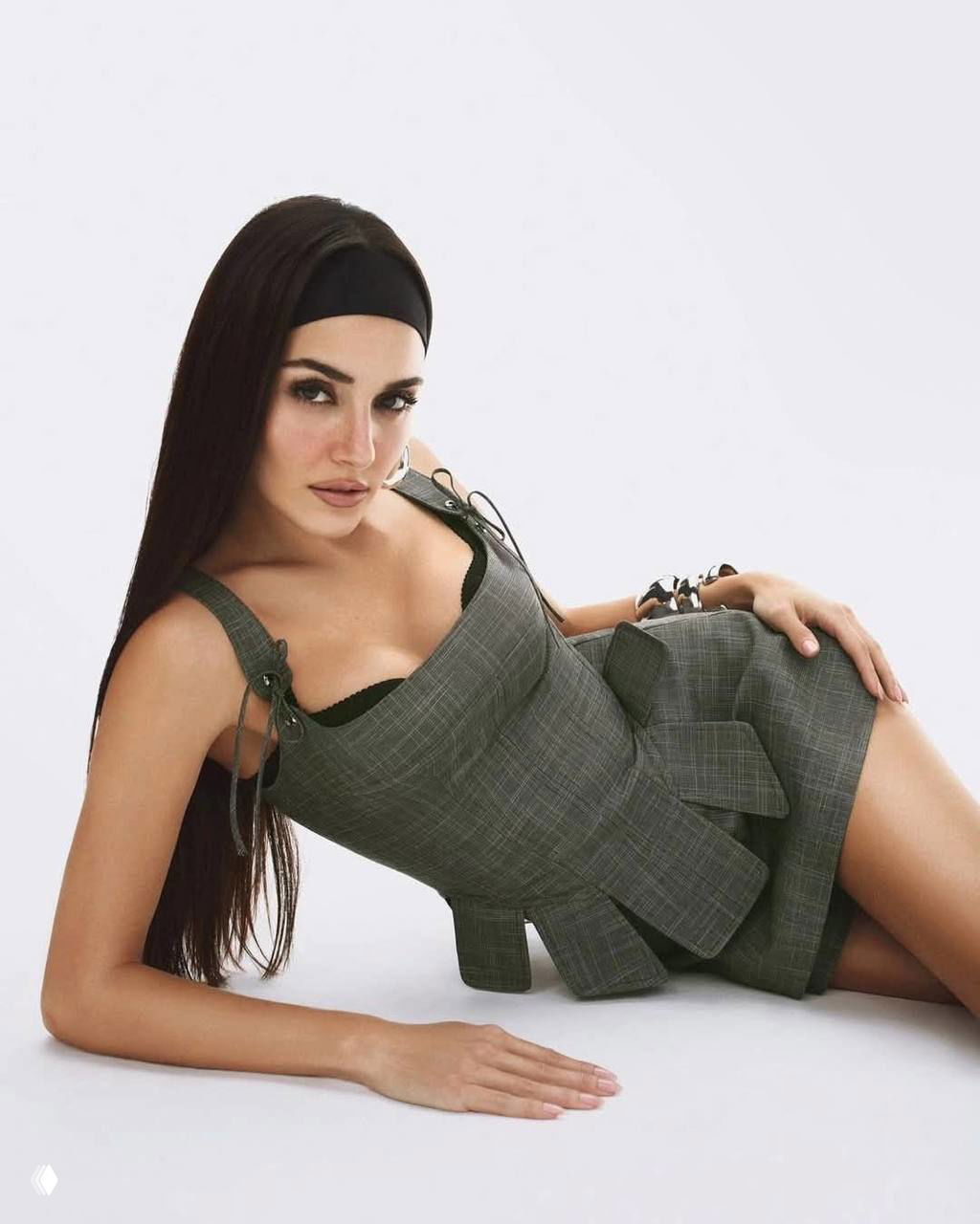 Женщина в сером платье в лежачей позе на светлом фоне, стильная постановка и гламурный макияж в студийной съёмке.