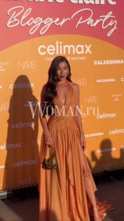 Карина Нигай на красной дорожке Marie Claire Blogger Party в платье кораллово-оранжевого оттенка на фоне бренд-баннера и логотипов спонсоров мероприятия