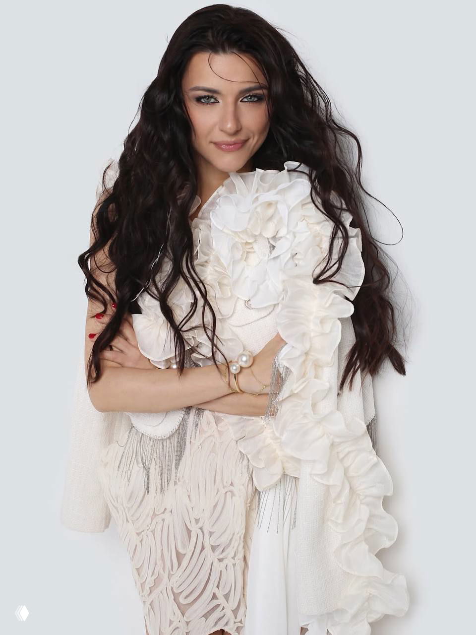 Студийный кадр женщины в белом платье с рюшами, взгляд в камеру, волнистые тёмные волосы и нейтральный фон создают образ «лебедя»