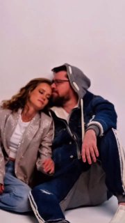 Гарик Харламов и Екатерина Ковальчук сидят рядом, облокотившись друг на друга и улыбаясь в повседневной одежде на светлом нейтральном фоне.