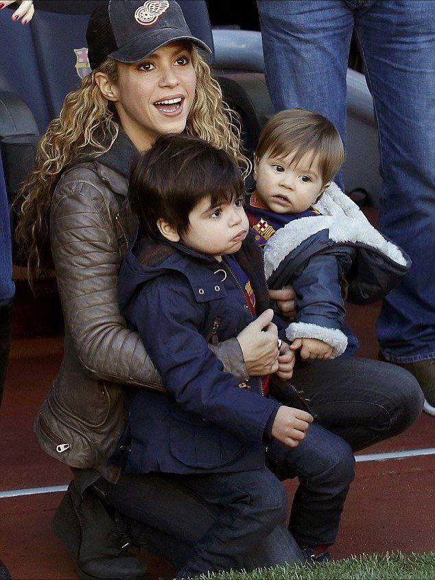 Женщина на спортивной трибуне держит младшего ребёнка на коленях, рядом старший сын, атмосфера матча и семейная поддержка.