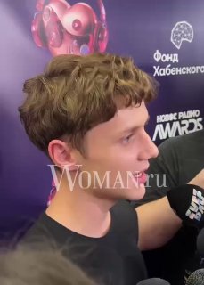 Портрет Вани Дмитриенко в профиль на фоне баннера премии «Новое радио AWARDS»: он даёт интервью, виден логотип Woman.ru.