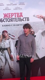 Молодой мужчина позирует на фоне постера фильма «Жертва обстоятельств» рядом с красной дорожкой и оформлением зоны показа премьеры.