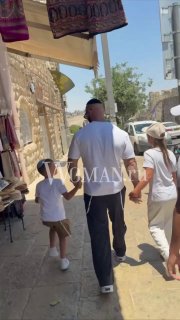 Прогулка по узкой улице старого города в Израиле: мужчина идёт, держась за руку с ребёнком; уличные прилавки и яркое солнце.
