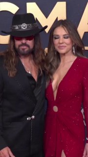 Вертикальное фото пары на красной дорожке: Элизабет и Билли Рэй стоят близко друг к другу, виден общий образ и улыбки — кадр в полноформатном вертикальном формате.