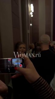 Зрители в коридоре киносалона записывают происходящее на телефоны; кадр показывает толпу, освещение и движение к залу во время премьеры.