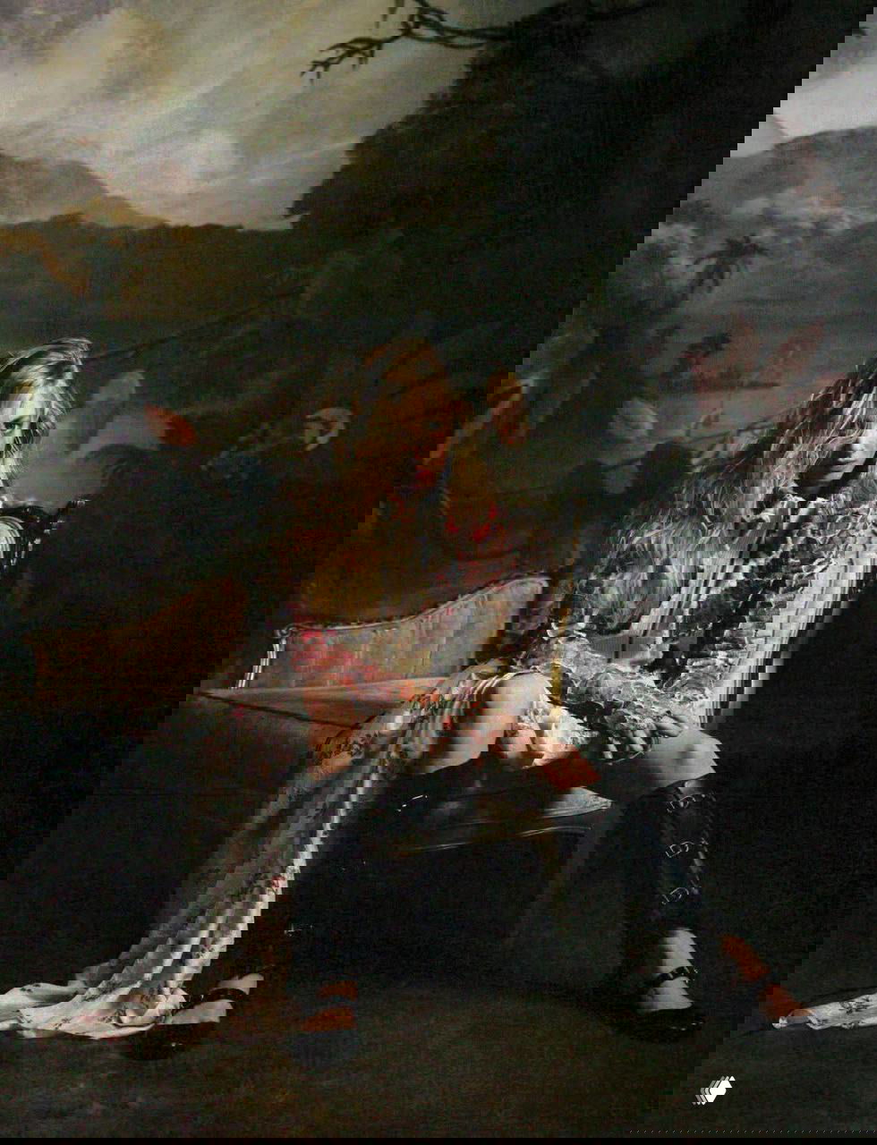 Студийный портрет: женщина в длинном платье и высоких ботинках сидит в кресле на фоне пасторальной живописи, кинематографичная палитра и постановка.