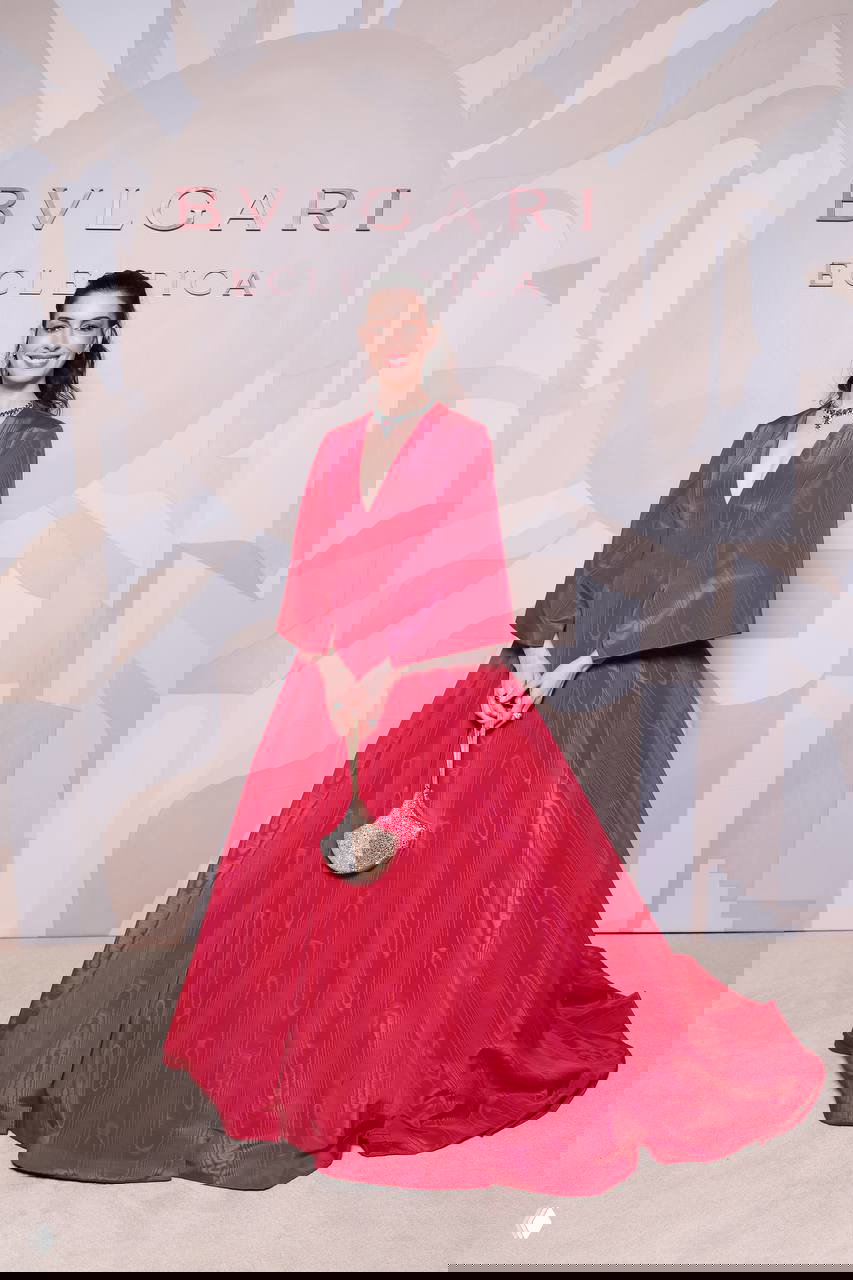 Энн Хэтэуэй в полный рост в платье розового цвета на фоне инсталляции Bvlgari Eclettica, видны платье и сумочка.