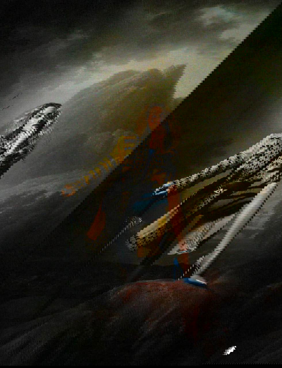 Фотокадр с костюмом в палитре жёлтого: женщина опирается на меч в постановочном пейзаже, стилизованная модная сцена с театральным фоном.