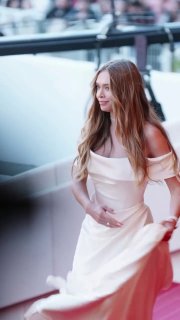 Вера Брежнева в белом эффектном платье на красной дорожке Каннского кинофестиваля, в полуповороте, фон — публика.
