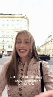 Селфи Анны Пересильд в светлой куртке на фоне городской застройки; актриса улыбается и смотрит в камеру, кадр вертикальный.