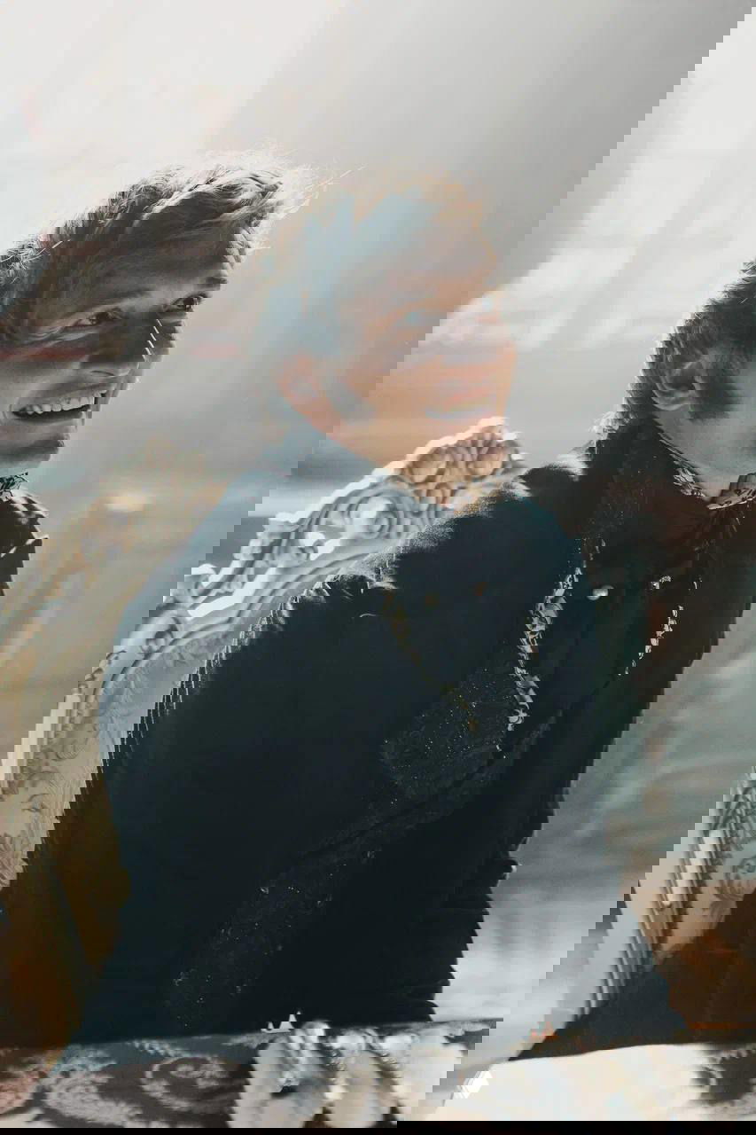 Матвей Лыков смеётся за столом в мягком боковом свете дворцовой сцены; на переднем плане элементы сервировки, подчёркивающие антураж съёмок.