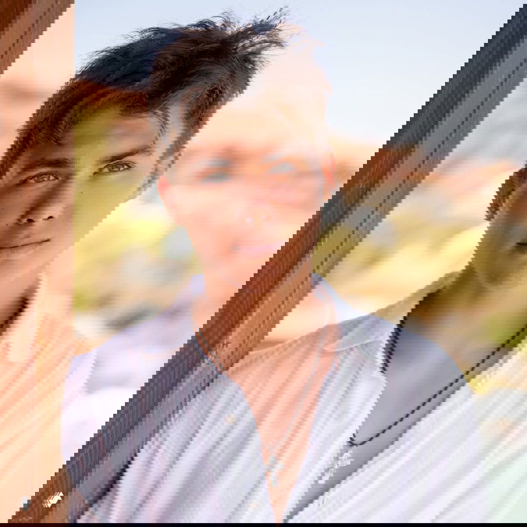 Крупный портрет старшего сына Матвея в белой рубашке на фоне размытых летних пейзажей и спокойного неба у воды.