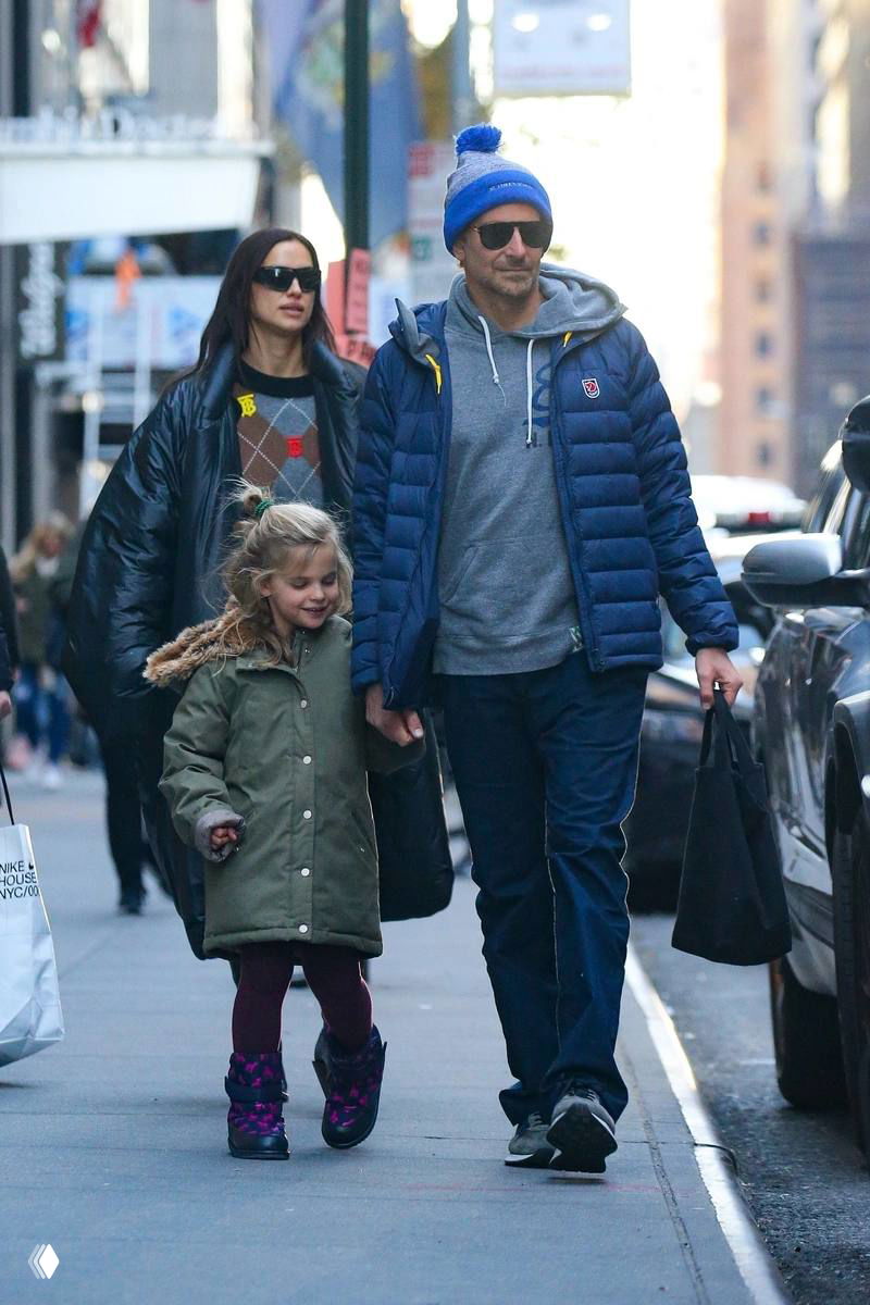 Мужчина в тёплой куртке и шапке держит девочку за руку во время прогулки по улицам города; изображение сделано с близкого расстояния.